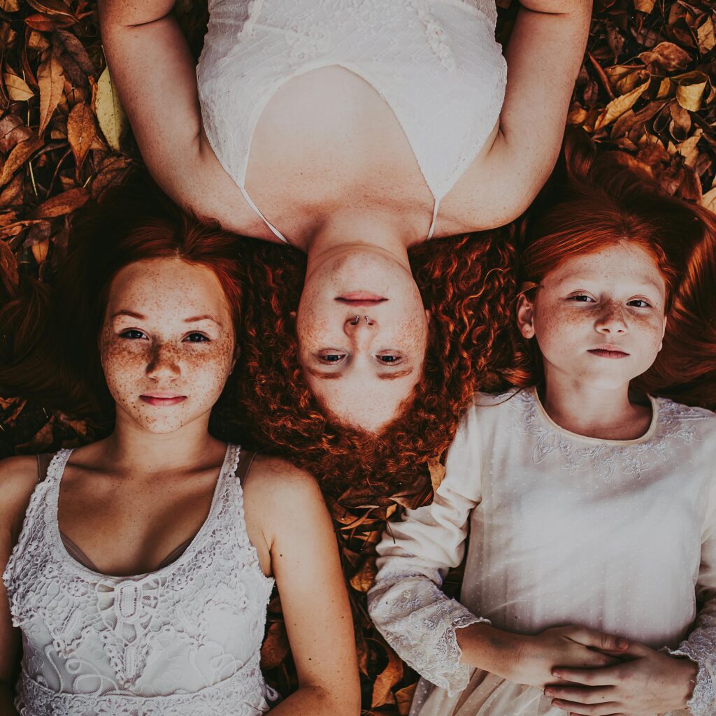 Three redheaded girls lying on autumn leaves, showcasing warmth and natural beauty.